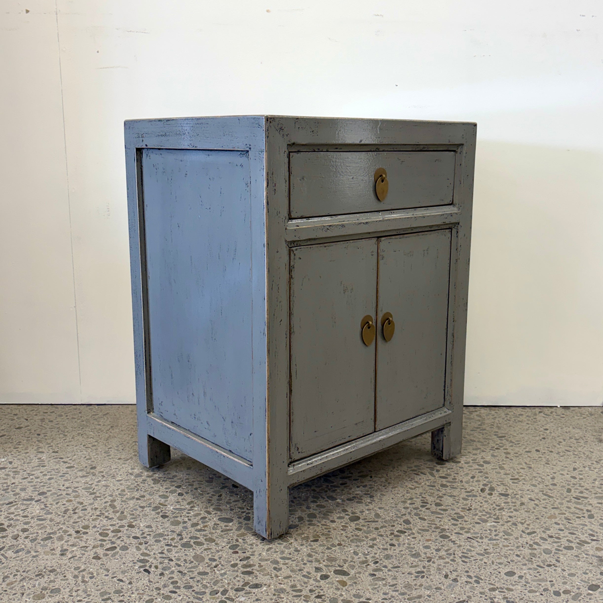 Angled view of Far East glossy grey bedside cabinet with drawer, two doors and brass handles