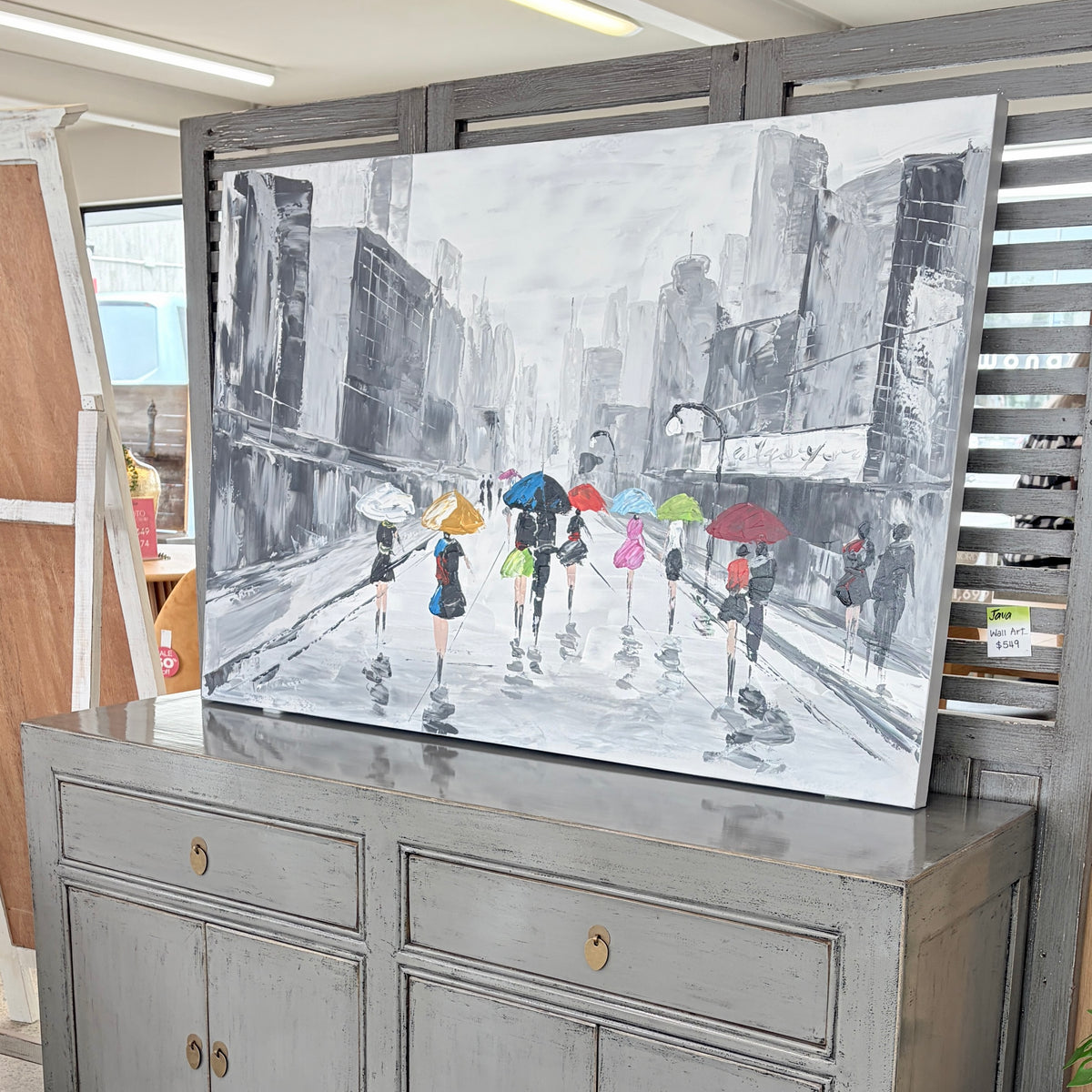 A Splash of Colour canvas painting displayed in a furniture showroom, featuring colourful umbrellas in a grey cityscape