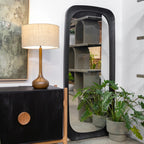Amalie Mirror in black styled as a full-length floor mirror beside a cabinet and indoor plants
