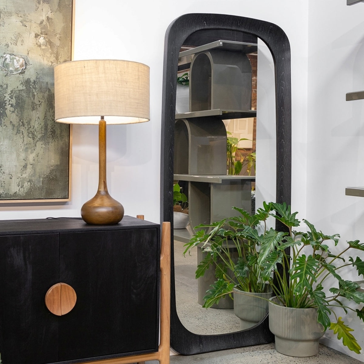 Amalie Mirror in black styled as a full-length floor mirror beside a cabinet and indoor plants