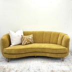 Bardot Sofa in Marigold featuring a curved silhouette, vertical channel detailing and textured fabric upholstery.