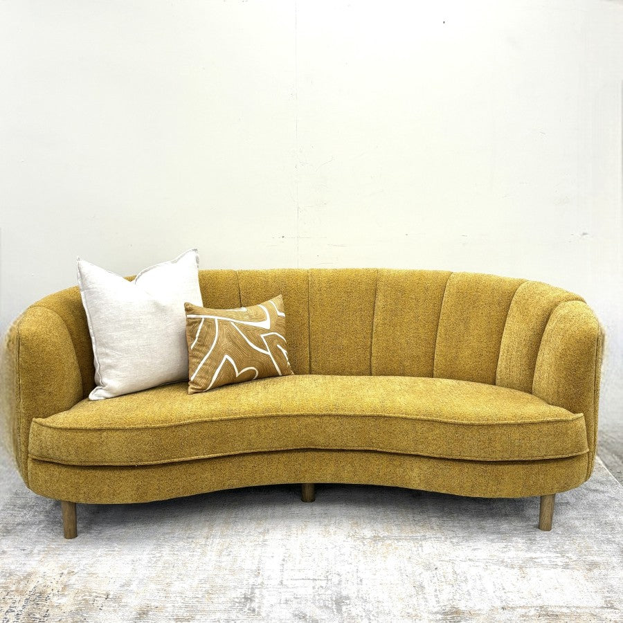 Bardot Sofa in Marigold featuring a curved silhouette, vertical channel detailing and textured fabric upholstery.