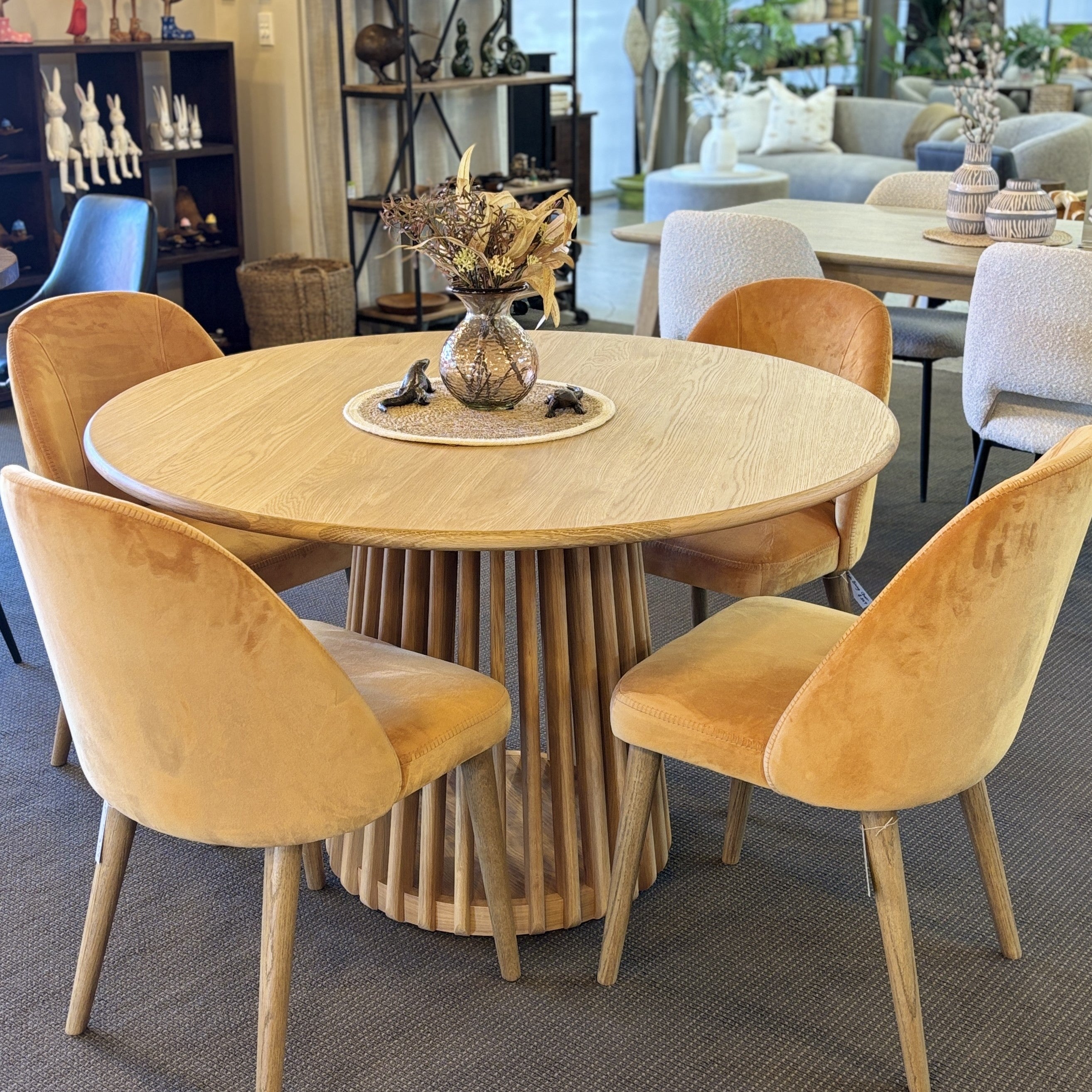The Bur Round Dining Table styled with dining chairs in a contemporary dining setting, highlighting its warm oak finish and inviting round shape.