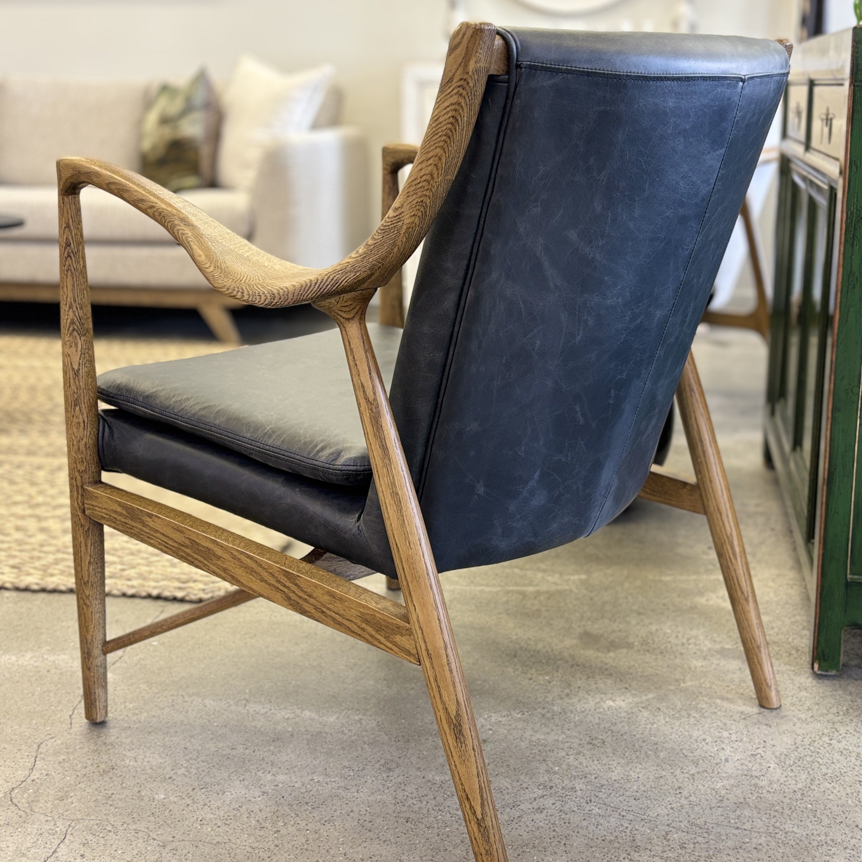 Rear view of the Coco Occasional Chair, showcasing the beautifully crafted timber frame and black leather backrest.