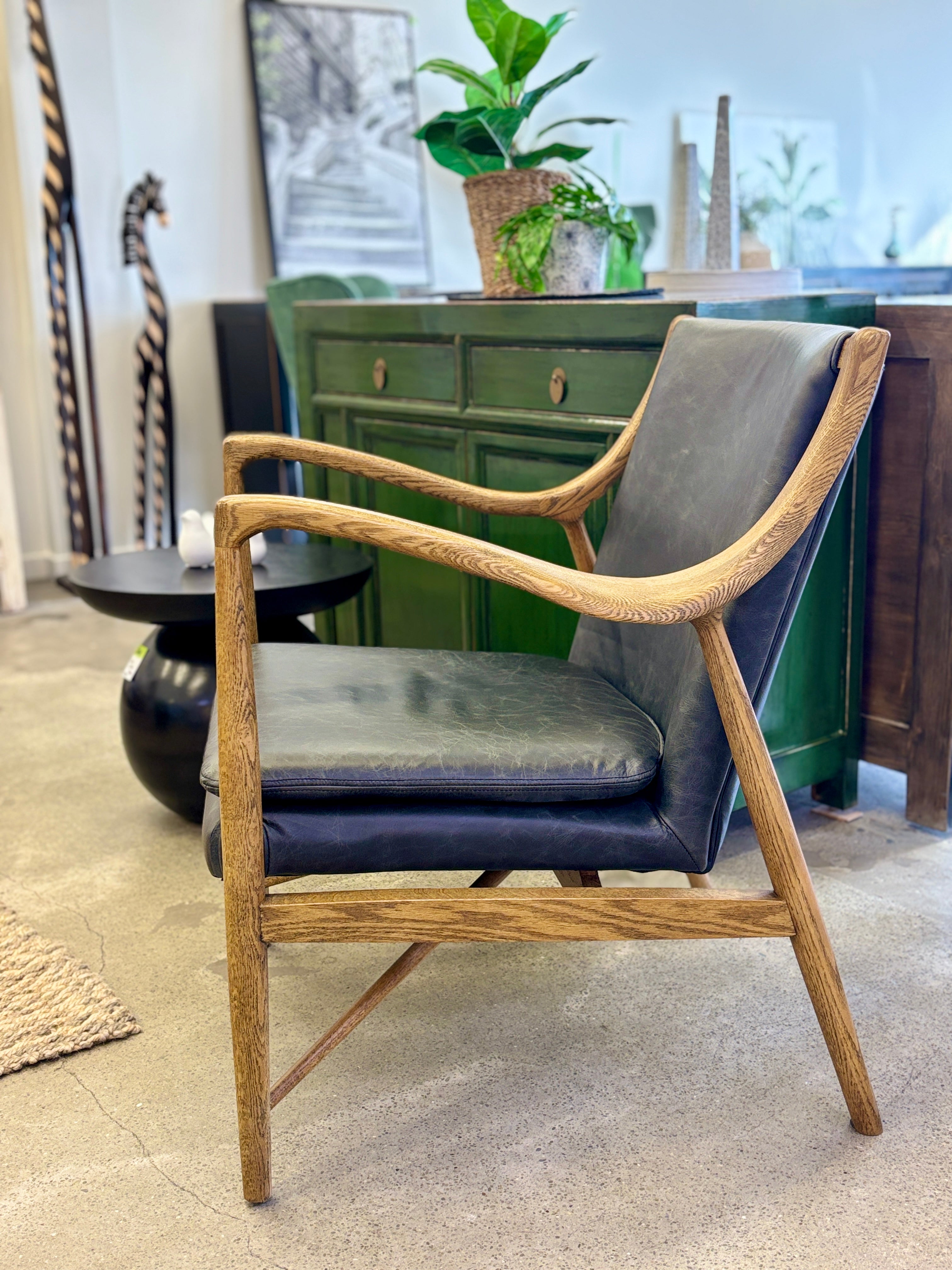 Side profile of the Coco Occasional Chair, showcasing its curved timber frame, supportive seat and premium black leather upholstery.