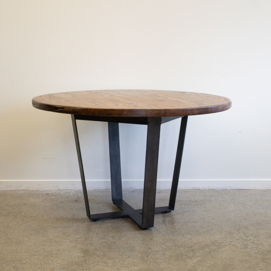 Side view of the Evolution Round Dining Table in Albany, highlighting the solid mango wood tabletop and contemporary iron leg design.