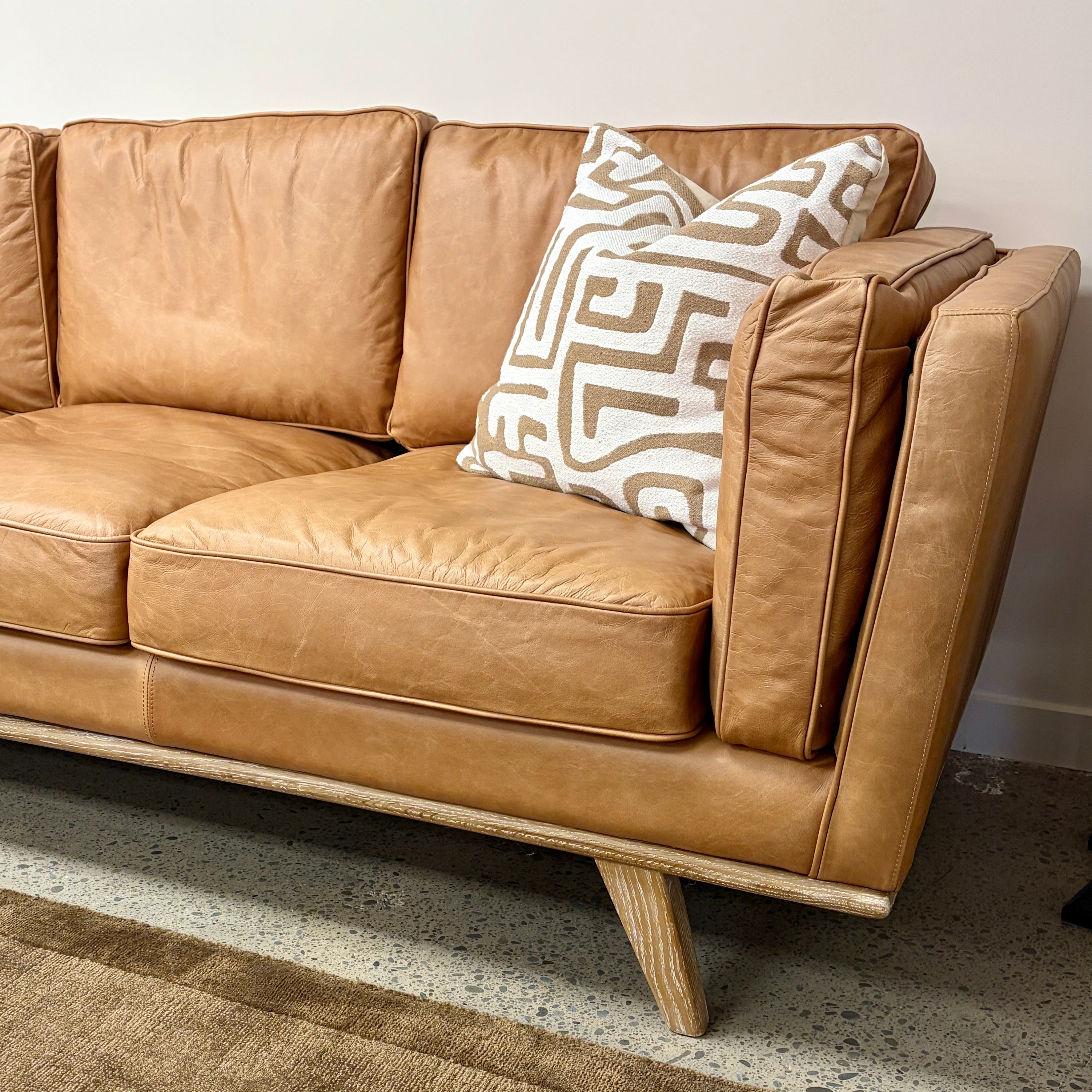 Angled view of the Fergus Sofa in Toffee leather, showcasing its contemporary silhouette, premium leather upholstery and oak legs.