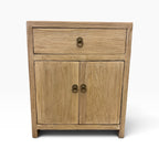 Front view of the Lydia Bedside in natural elm with one drawer, two doors and brass-style ring handles