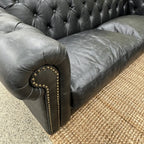 Close-up of the Maxwell Chesterfield sofa's rolled arm with deep button tufting and premium black leather.