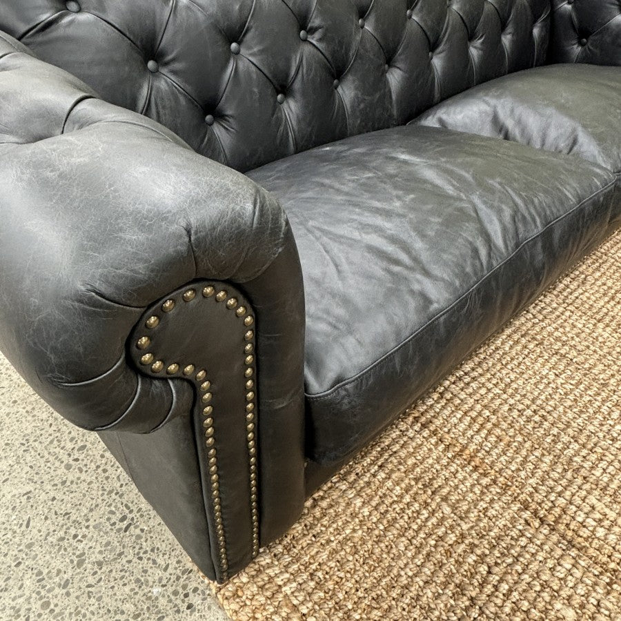 Close-up of the Maxwell Chesterfield sofa's rolled arm with deep button tufting and premium black leather.