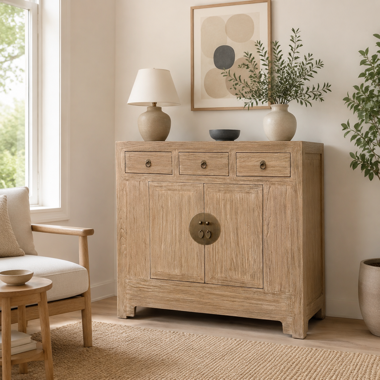 Sunny sideboard in Natural Elm with three drawers and two cabinet doors, styled in a bright, modern room with a lamp, framed art, and plants.